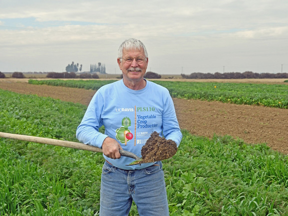 A man holding a shovel full of dirt, with a field in the background.