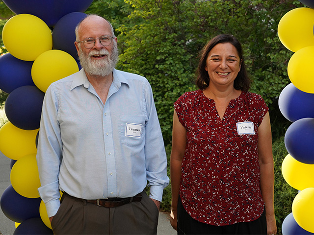 A woman and a man, smiling. Yellow and blue balloons are next to them.