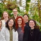 A group of young people in a greenhouse with tall leafy plants.